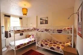 Bright dormitory with two sets of white metal bunk beds, spotted duvets and a window.