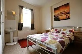 Private double room with a metal-framed double bed, spotted duvet, bedside lamps and a sunset canvas on the wall.